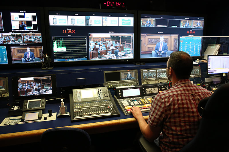 broadcast operator seated at desk in front of audio board and several screens