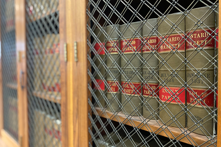 Ontario Gazette books behind a metal wire mesh in a wooden cabinet.