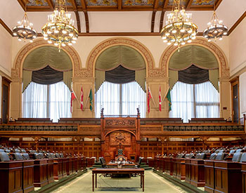 view of the chamber from the back of the room looking towards the Clerk's table and Speaker's dais with three large windows behind