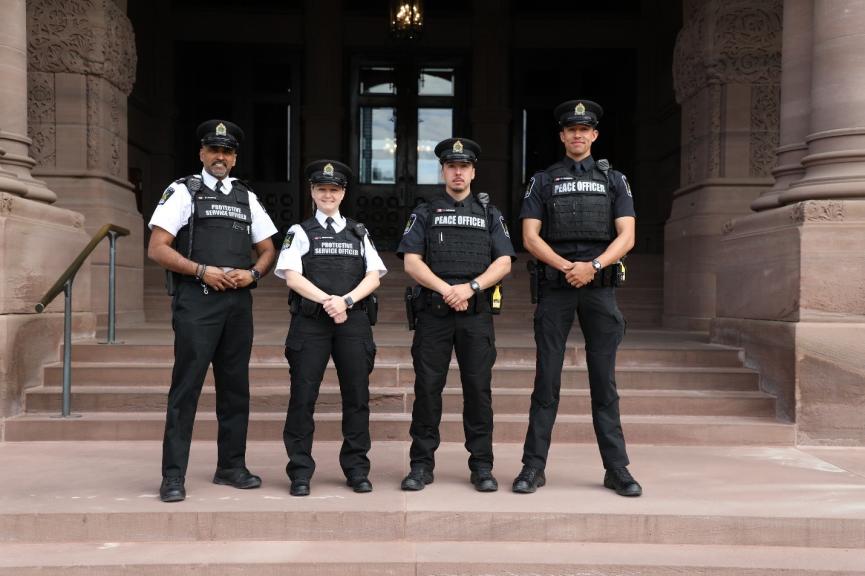 Une agente et un agent de sécurité et deux agents de la paix en face de l’Assemblée législative de l’Ontario.